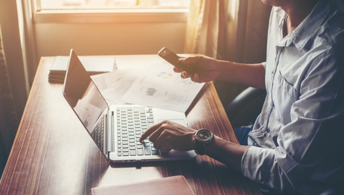 Businessman hands using cell phone with laptop at office desk.